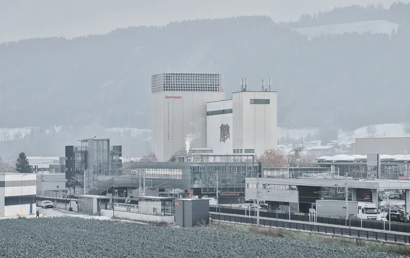Industrial complex with concrete tower and perforated parapet set against misty forested hills in winter