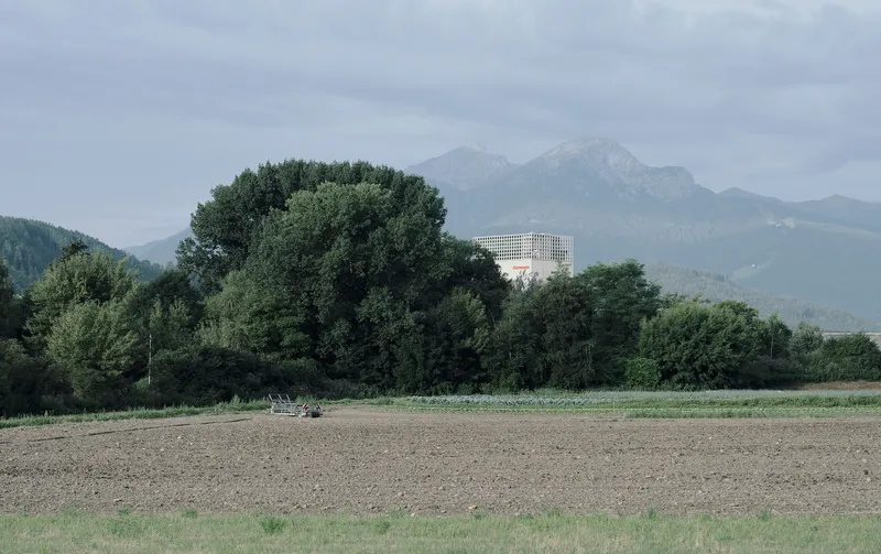 Distant view of the tower with latticed crown emerging behind dense tree line and plowed fields