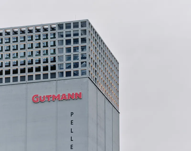 Corner view of the concrete podium and gridded glass facade above under an overcast sky
