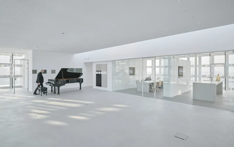 White terrazzo floor and glass-walled room with a person seated at the piano by the windows