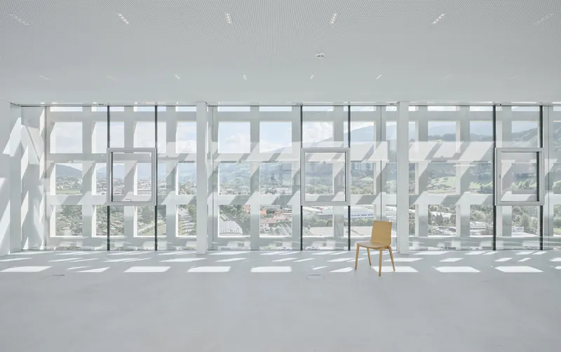 Single wooden chair facing the perforated white screen wall and full-height glazing beyond