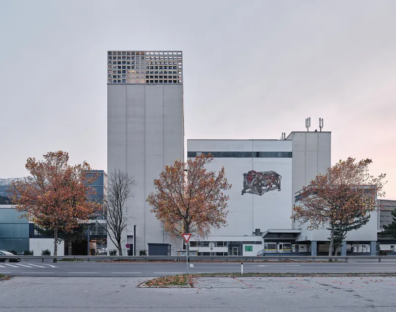 Street view of the concrete tower with perforated metal crown and bull mural flanked by autumn trees