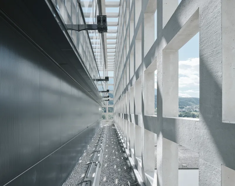 Narrow rooftop passage between metal wall panels and concrete light screen with gravel floor