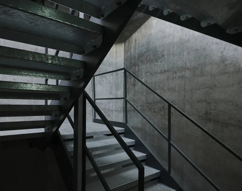 Metal staircase with perforated treads against board-formed concrete wall in shadowed stairwell