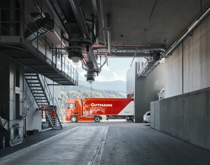 Covered loading bay with exposed concrete ceiling, steel walkway, and red delivery truck framed by mountain view