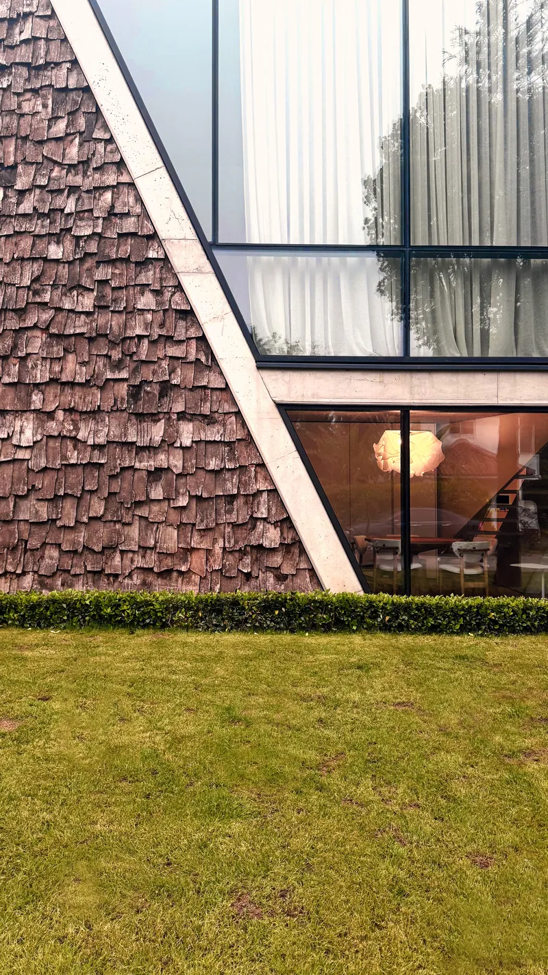 Wood shingle facade with horizontal glazing bands above a manicured lawn at dusk with interior lights on