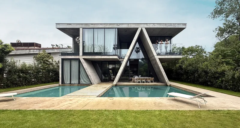 Garden facade with angled concrete supports framing a swimming pool and timber deck under overcast sky