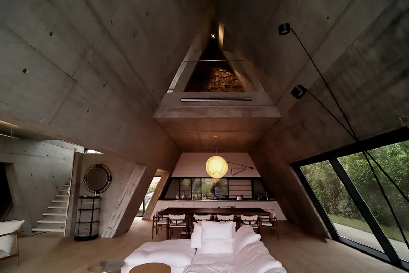 Interior view up into the triangular vaulted ceiling with exposed concrete and pendant light above dining area