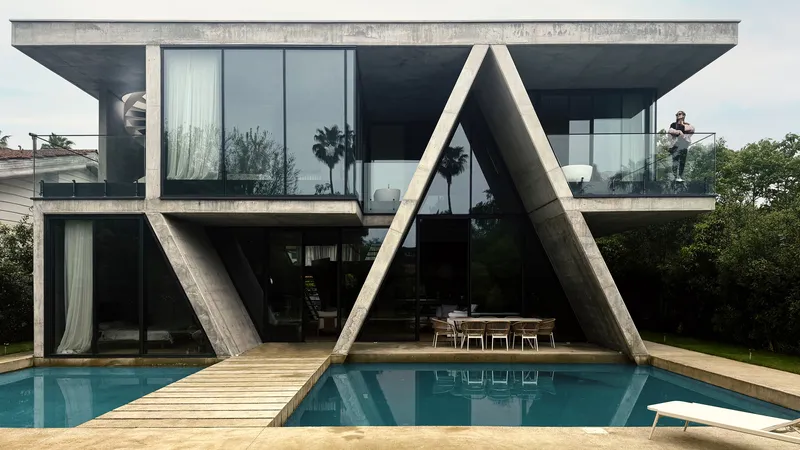 Rear elevation showing the angled concrete columns reflected in the swimming pool with timber bridge crossing water