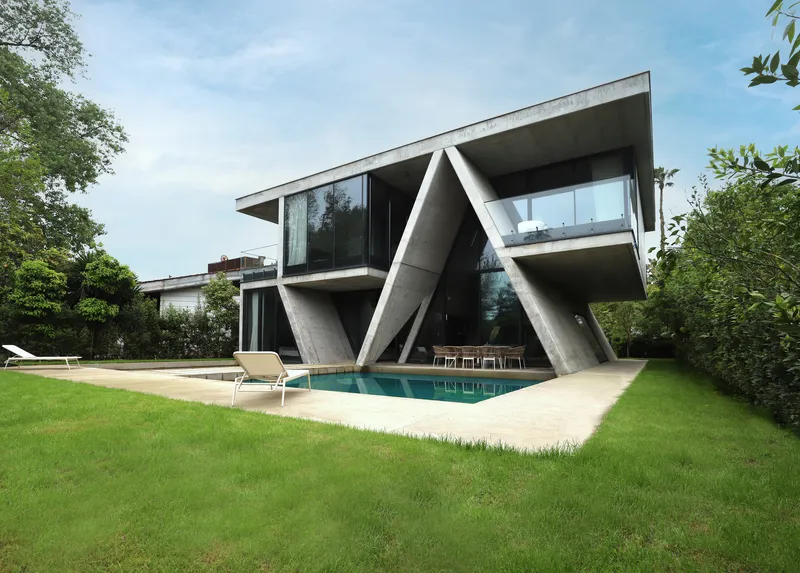 Oblique view of the cantilevered concrete structure above swimming pool surrounded by green lawn and trees