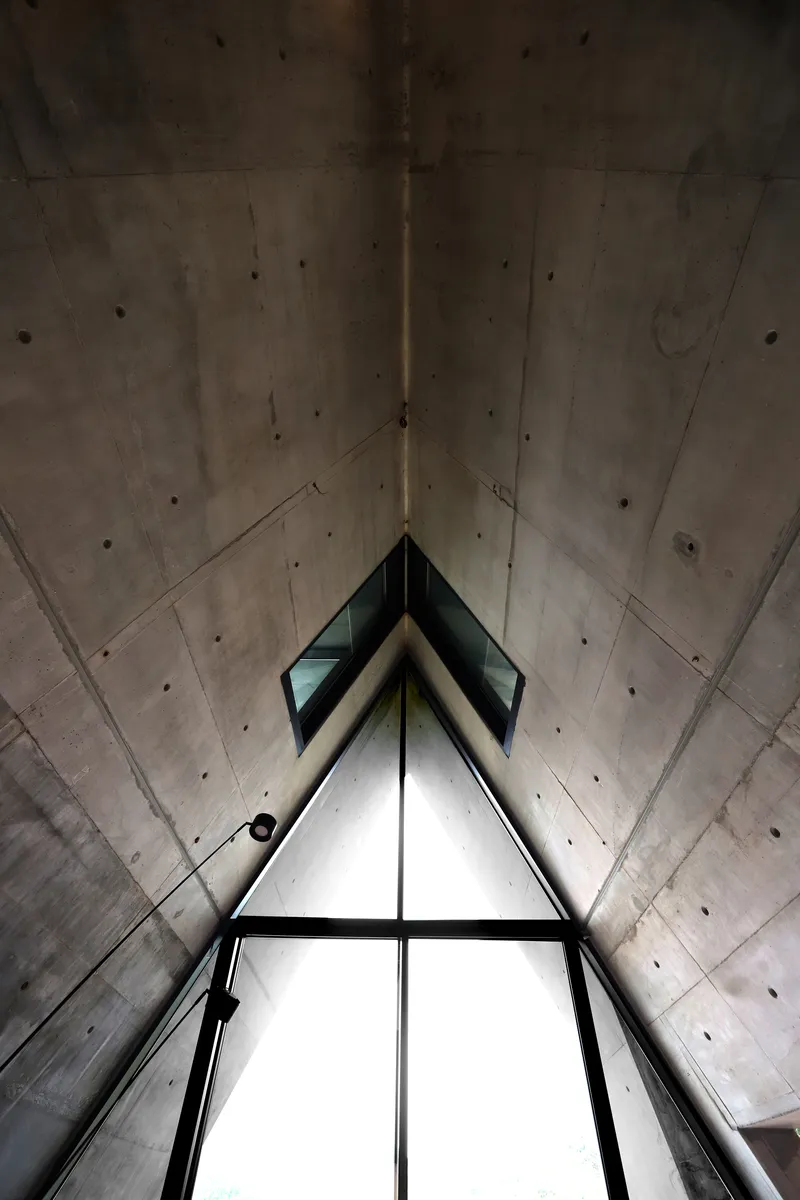 Looking up through the triangular skylight framed by angled concrete walls with visible formwork tie marks