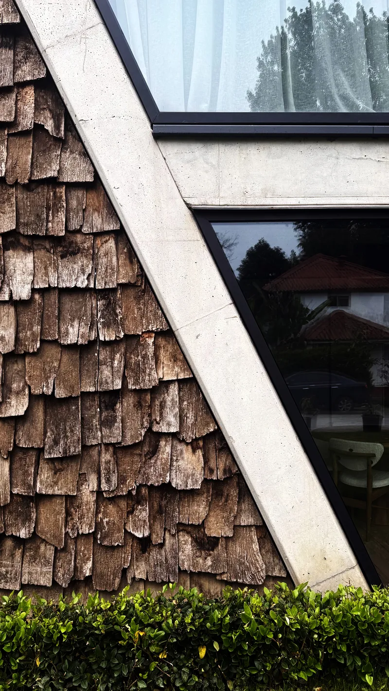 Exterior facade detail showing weathered wood shingle cladding meeting a concrete edge below horizontal windows