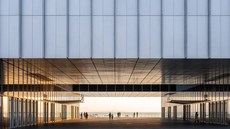 Ground-level view through the elevated volume showing timber-clad soffit and vertical metal fins at dusk