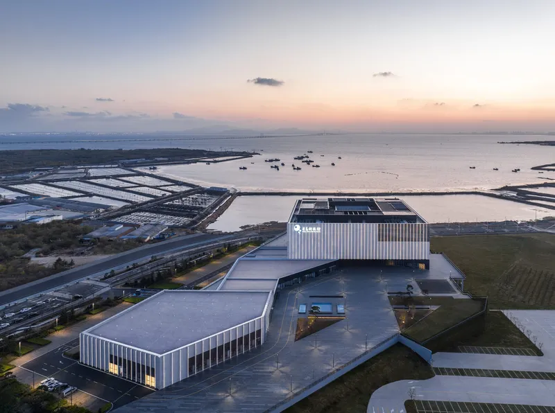 Aerial view of the paired volumes and plaza beside coastal wetlands at sunset