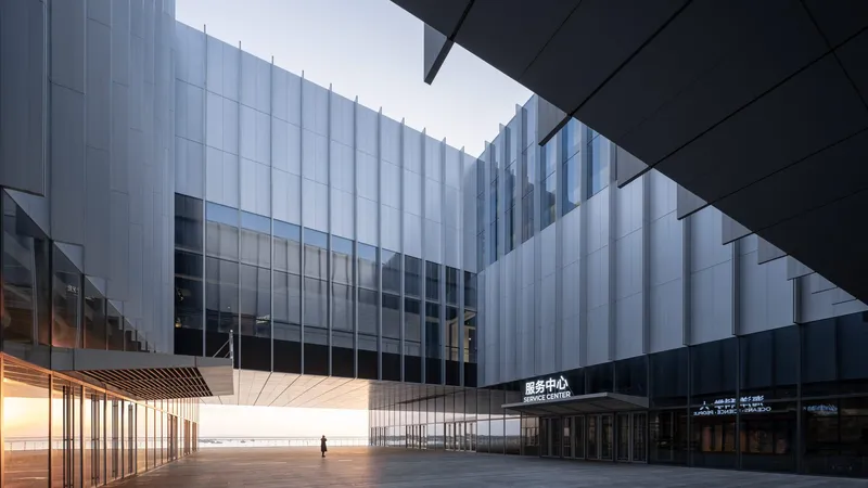 Covered plaza between translucent ribbed facades and illuminated timber soffit at twilight