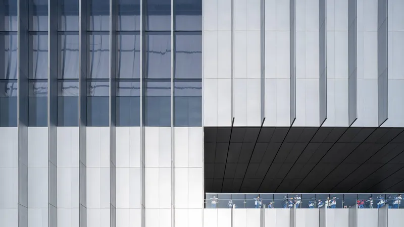 Facade detail showing white vertical panels meeting black soffit with glazed gallery strip revealing visitors inside