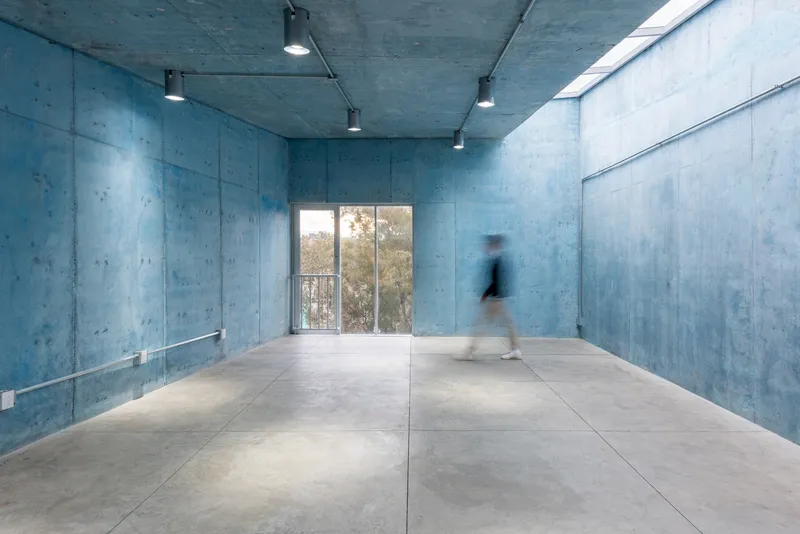 Concrete hall with polished floor and a person walking toward the glazed opening framing trees outside
