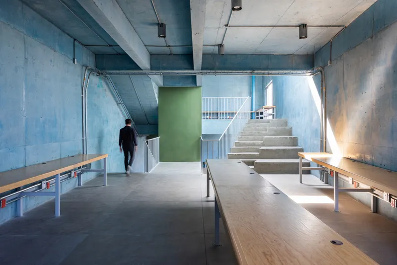 Interior view showing concrete stair rising toward upper level with timber benches and a figure departing below