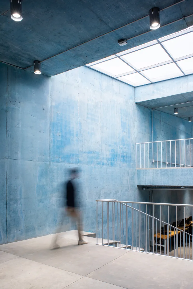 Multi-level atrium with blue concrete walls, metal railings and a blurred figure on polished floor