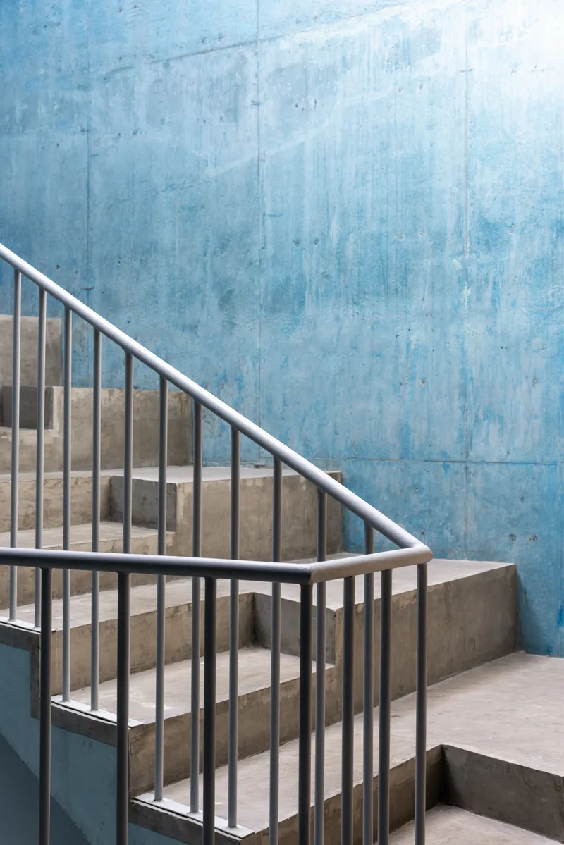 Close-up of staircase corner with metal railing against weathered blue concrete wall