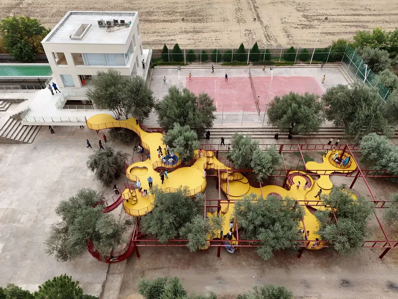 Aerial view of yellow curving playground platforms with red mesh railings woven among olive trees