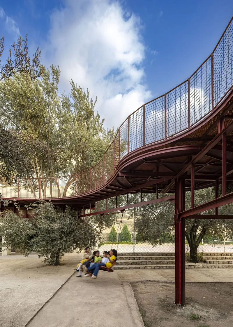 Curving canopy with mesh screens and red steel columns sheltering a stepped amphitheater among olive trees