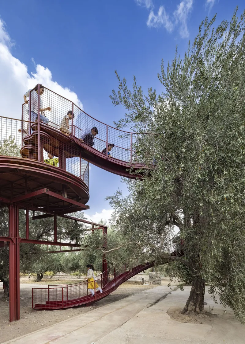 Steel observation tower with children on upper platform and mesh railings among olive trees