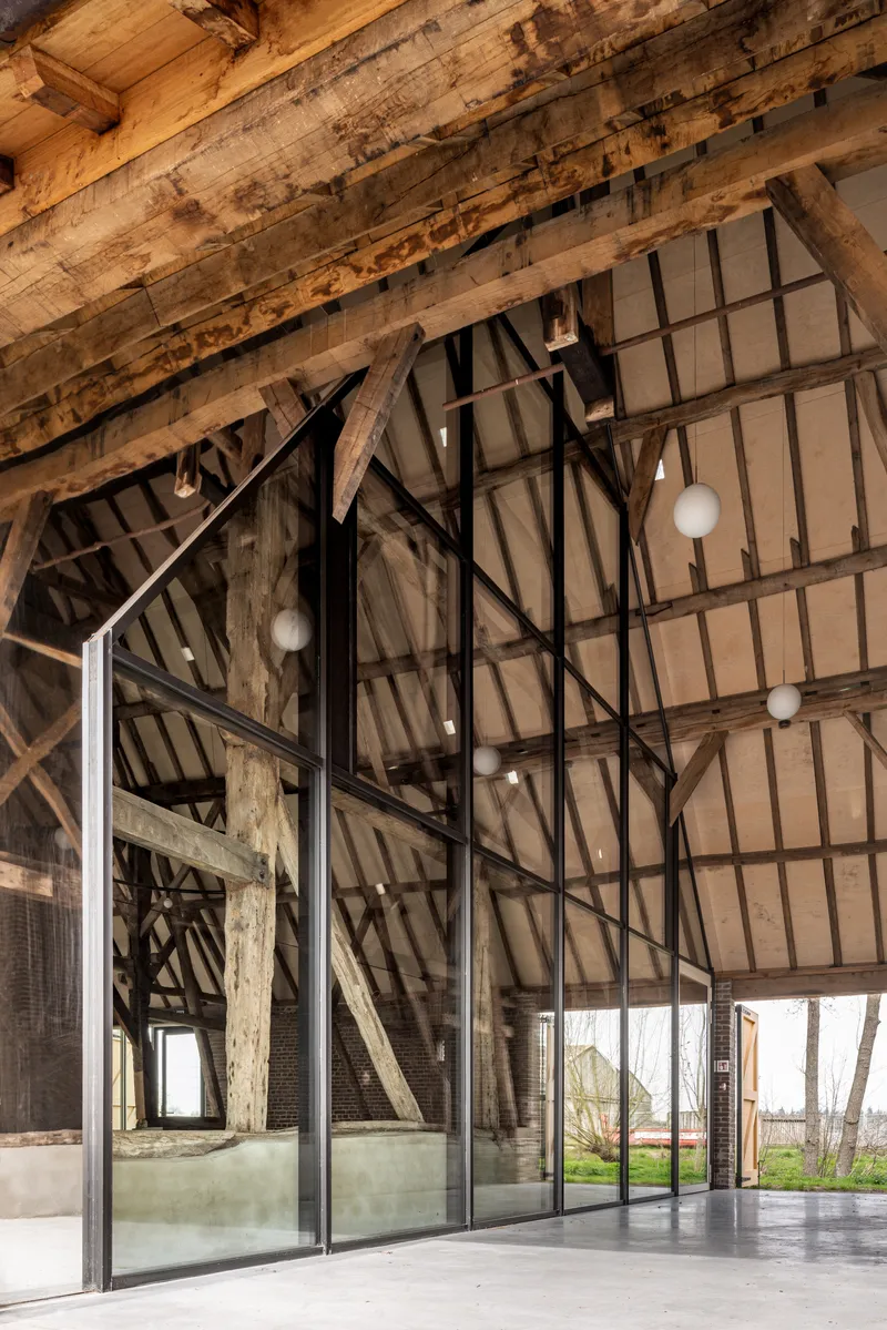 Glass wall with black steel framing reflecting timber roof structure and looking toward the landscape beyond