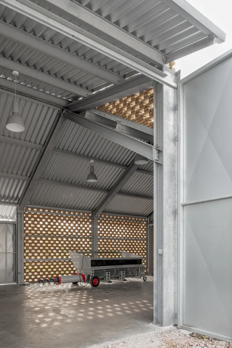 Interior workspace with corrugated metal ceiling, perforated brick screens, and polished concrete floor with machinery cart