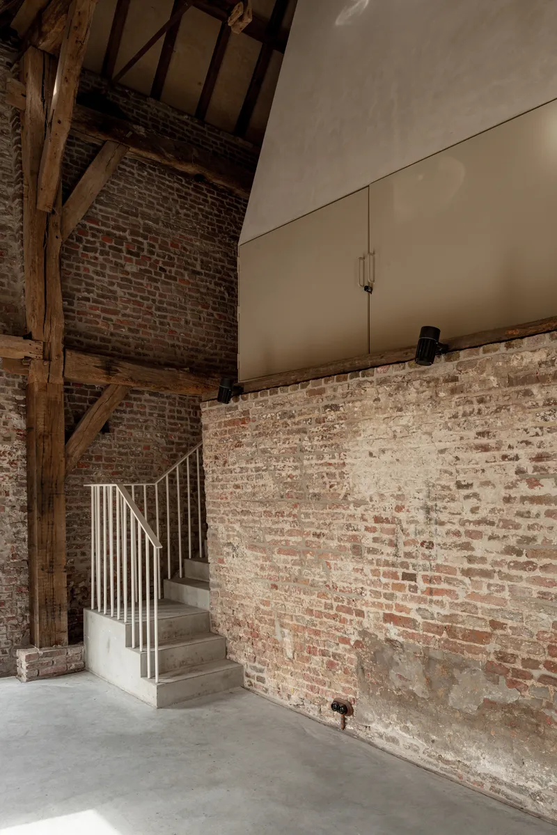 Concrete and steel staircase with white balustrade against exposed brick wall and timber roof beams