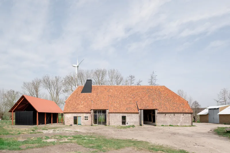 Cluster of brick volumes with orange tile roofs and a wind turbine in the background