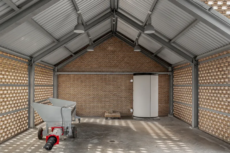 Gabled barn interior with perforated brick walls casting dappled light on the concrete floor