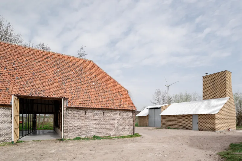 Courtyard view showing brick barn with orange tile roof and perforated brick tower with wind turbine beyond