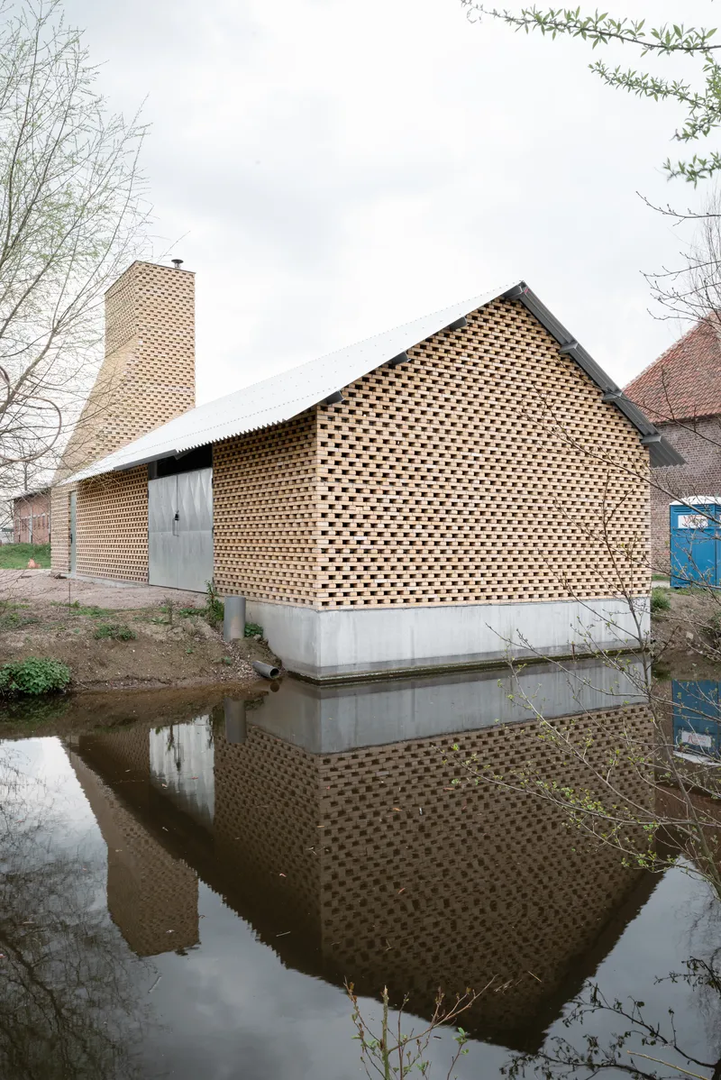 Gabled volume with perforated brick facade on concrete base reflected in adjacent canal water
