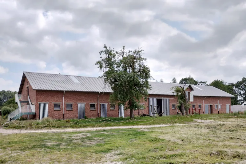 Brick barns with corrugated metal roofs and vertical striped shutters surrounding a courtyard with mature tree