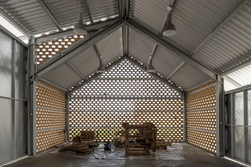 Interior workshop space with perforated brick walls filtering daylight through corrugated metal ceiling