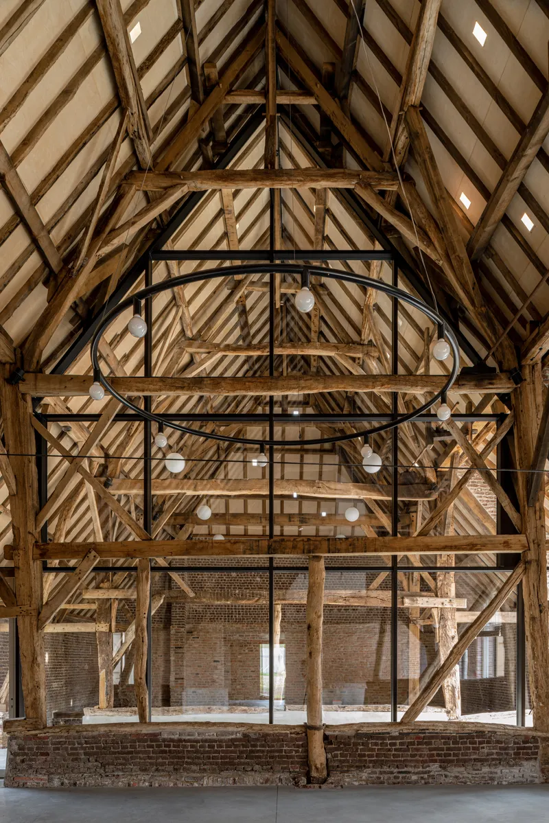 Exposed timber roof trusses and bracing with black steel circular walkway in renovated barn interior