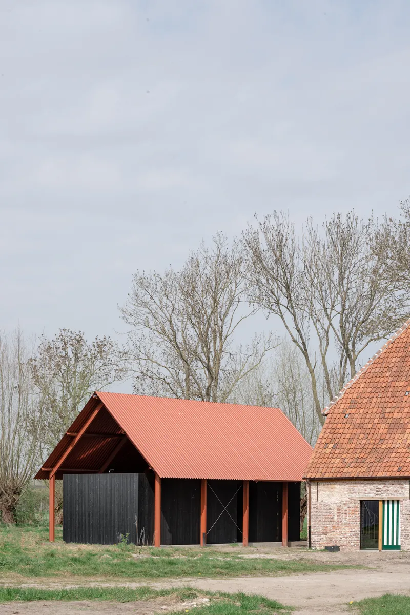 Side view of the coral-roofed barn structure with bare trees visible in the background