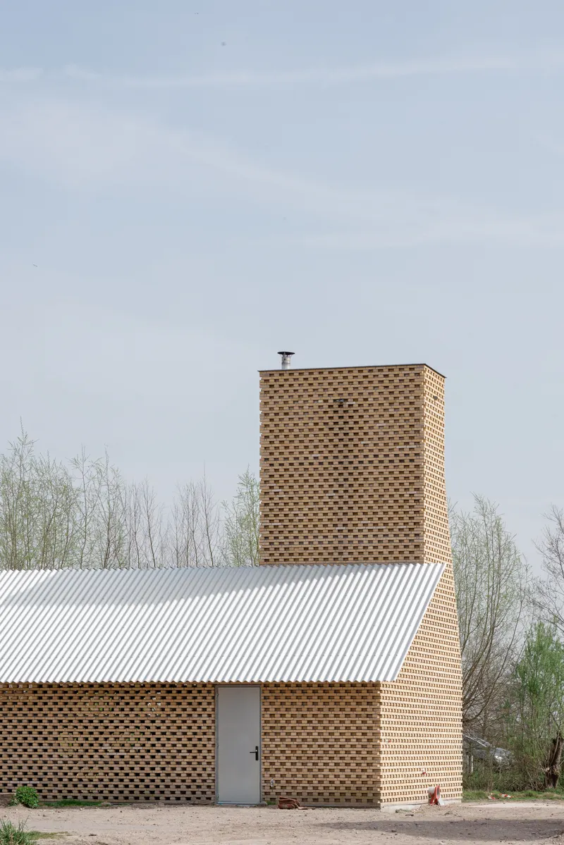 Perforated brick chimney rising above a corrugated metal roof beneath a pale spring sky
