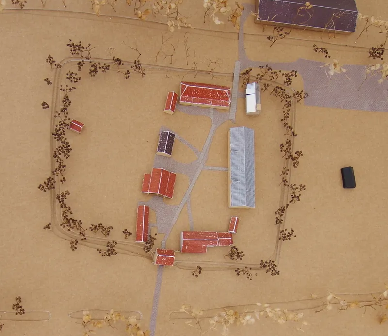 Aerial view of farm buildings arranged along paths in a sandy clearing with scattered trees