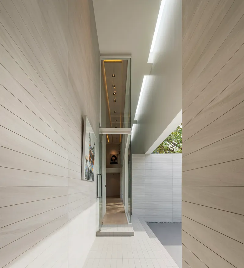 Narrow outdoor corridor between horizontal-tiled walls with a glazed ceiling slot and sunlight
