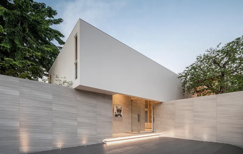 Entry courtyard with horizontal ribbed wall panels and recessed timber doorway beneath white upper volume