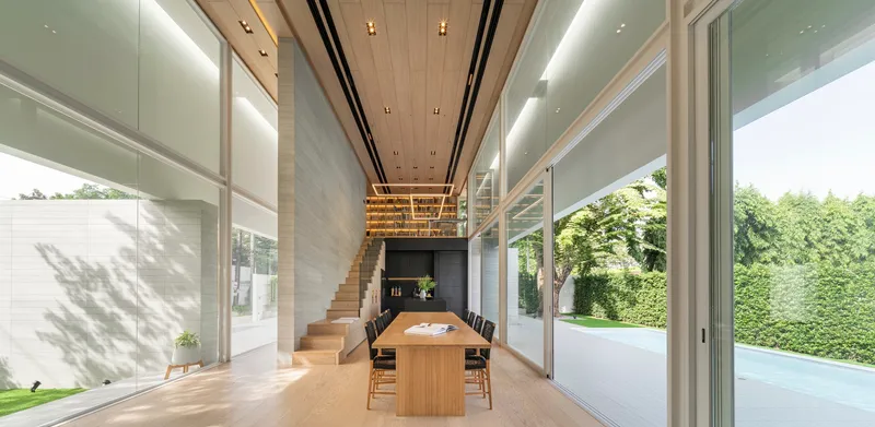 Double-height dining space with timber staircase and slatted ceiling under indirect lighting