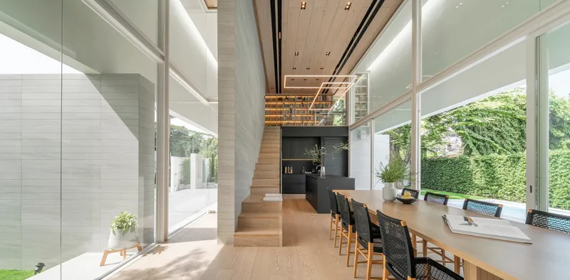 Living and dining space with floor-to-ceiling glazing opening onto lawn and hedge beyond
