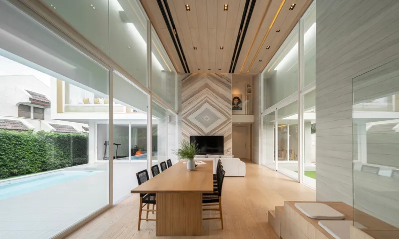 Double-height dining space with timber ceiling, chevron-patterned fireplace wall and floor-to-ceiling glass overlooking the lawn