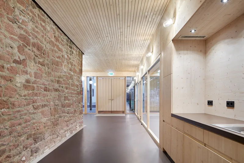 Hallway with exposed brick wall, timber cabinetry and slatted ceiling under daylight