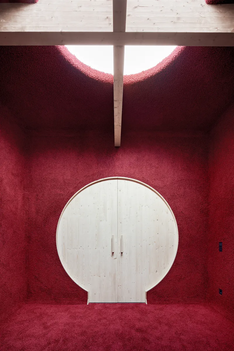 Circular plywood cabinet against deep red carpeted walls beneath a clerestory cross