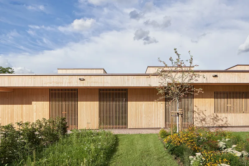 Light timber facade with vertical slatted screens and planted bed with flowering perennials