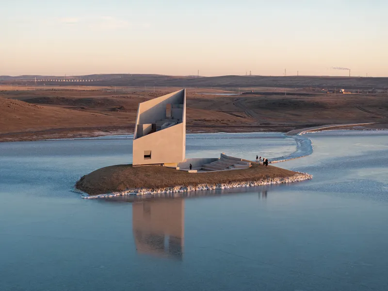 Angular white concrete chapel on a peninsula in a reservoir at sunset