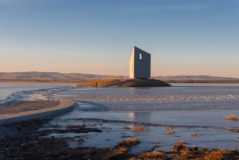 The angled facade with a single vertical window on the rocky outcrop at dusk